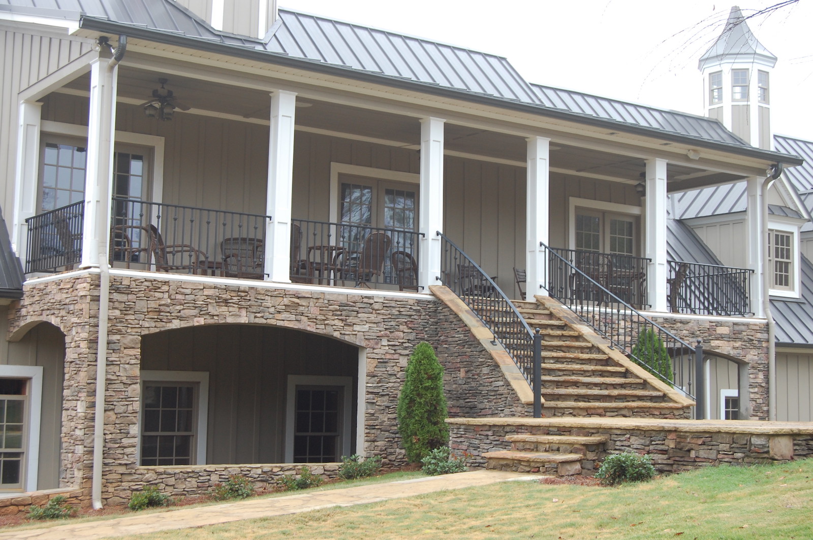 Black iron porch and stair railings on a two-story home with a stone lower level, built by Fabco Fabrications
