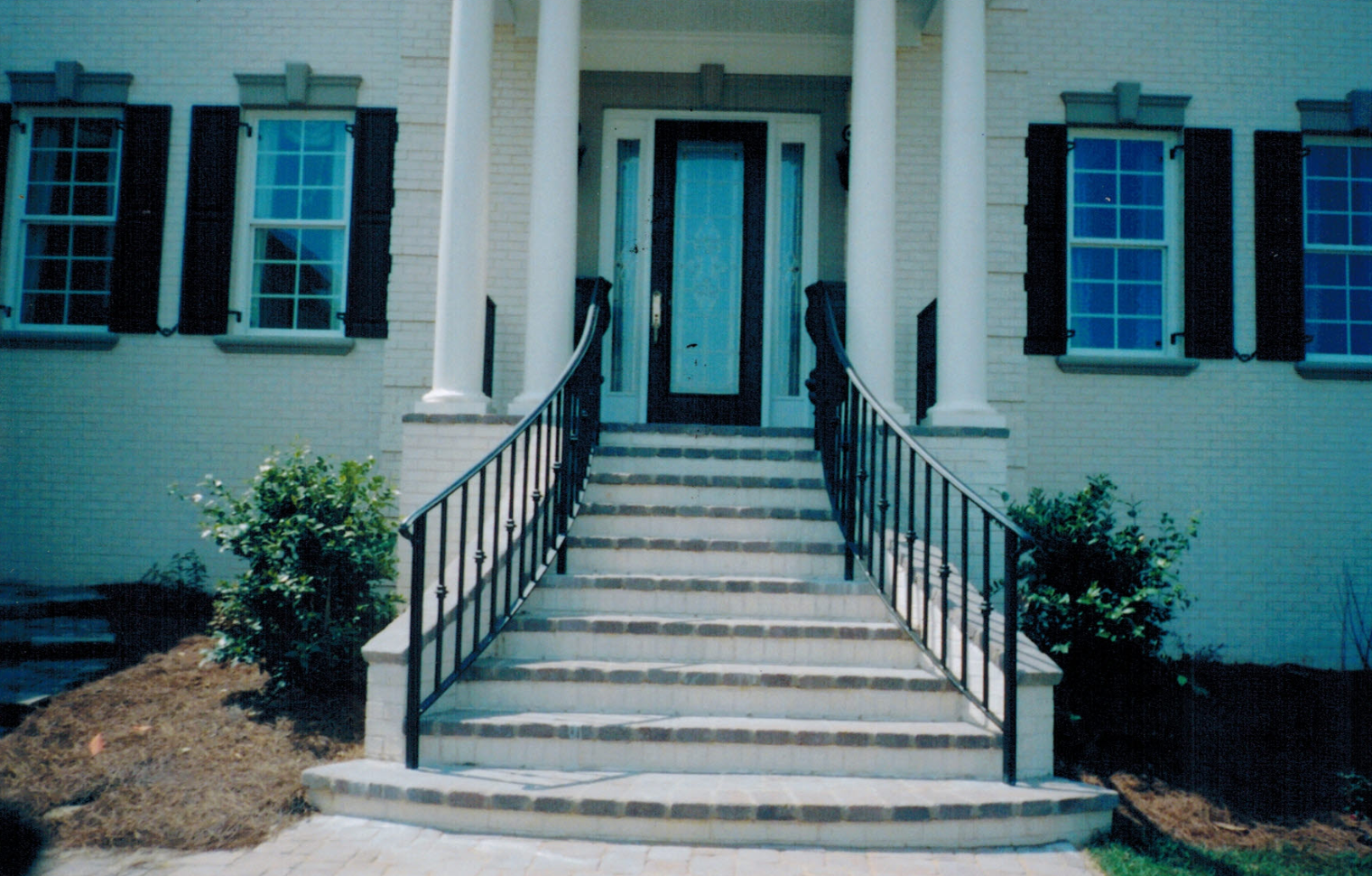 Black iron railings on both sides of front steps to a columned entry, a custom metal railing by Fabco Fabrications