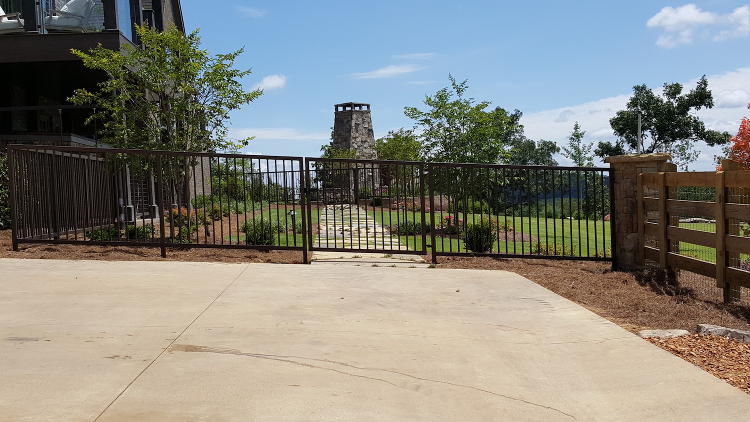 Black ornamental iron fence with a gate along a concrete patio, custom fencing by Fabco Fabrications